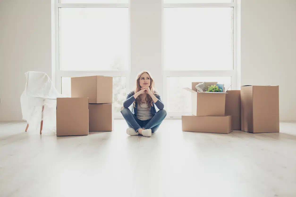 A woman sits on the floor of a bright, empty room contemplating moving back to her hometown