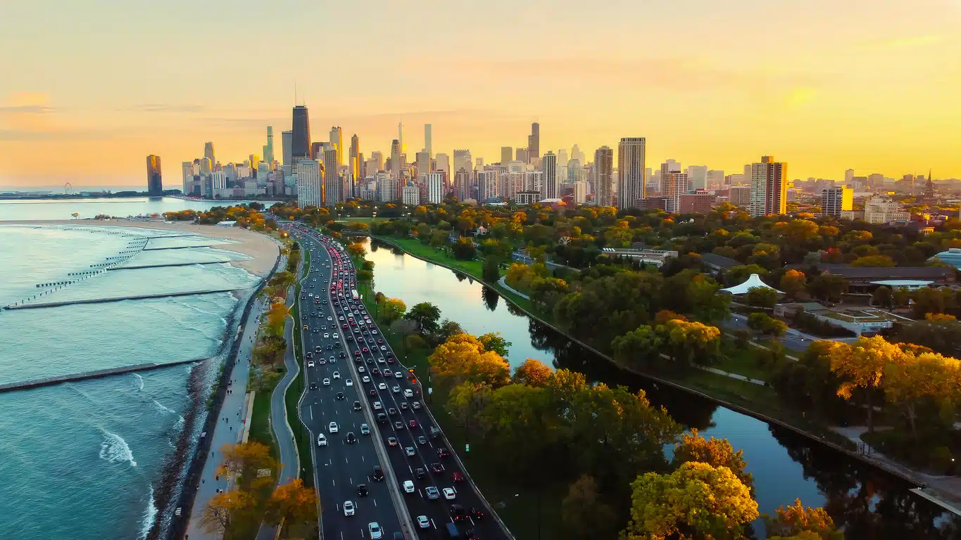 Aerial view of a coastal highway and park leading toward the Chicago city skyline during a golden sunset