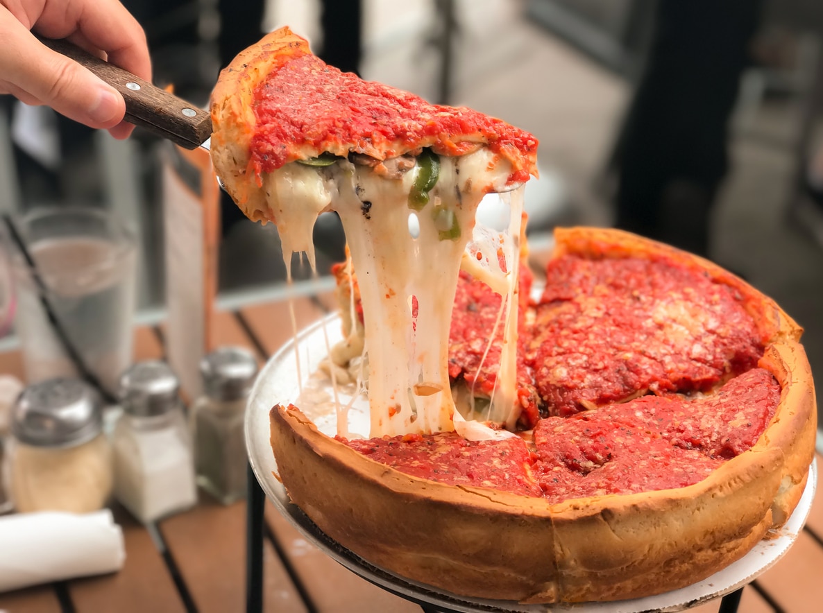 A metal server lifts a thick slice of deep-dish pizza, a popular food option for those moving from Atlanta to Chicago