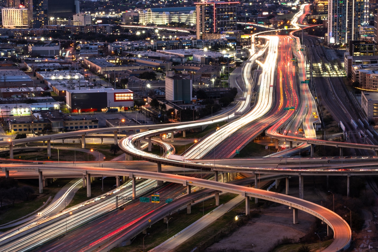 Long-exposure aerial shot of a Dallas freeway interchange at night, with bright streaks of light from moving traffic