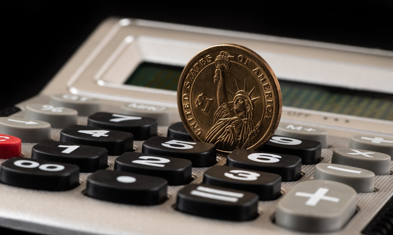 A gold $1 coin balanced on a desk calculator, symbolizing calculating the cost of living in San Francisco vs. NYC