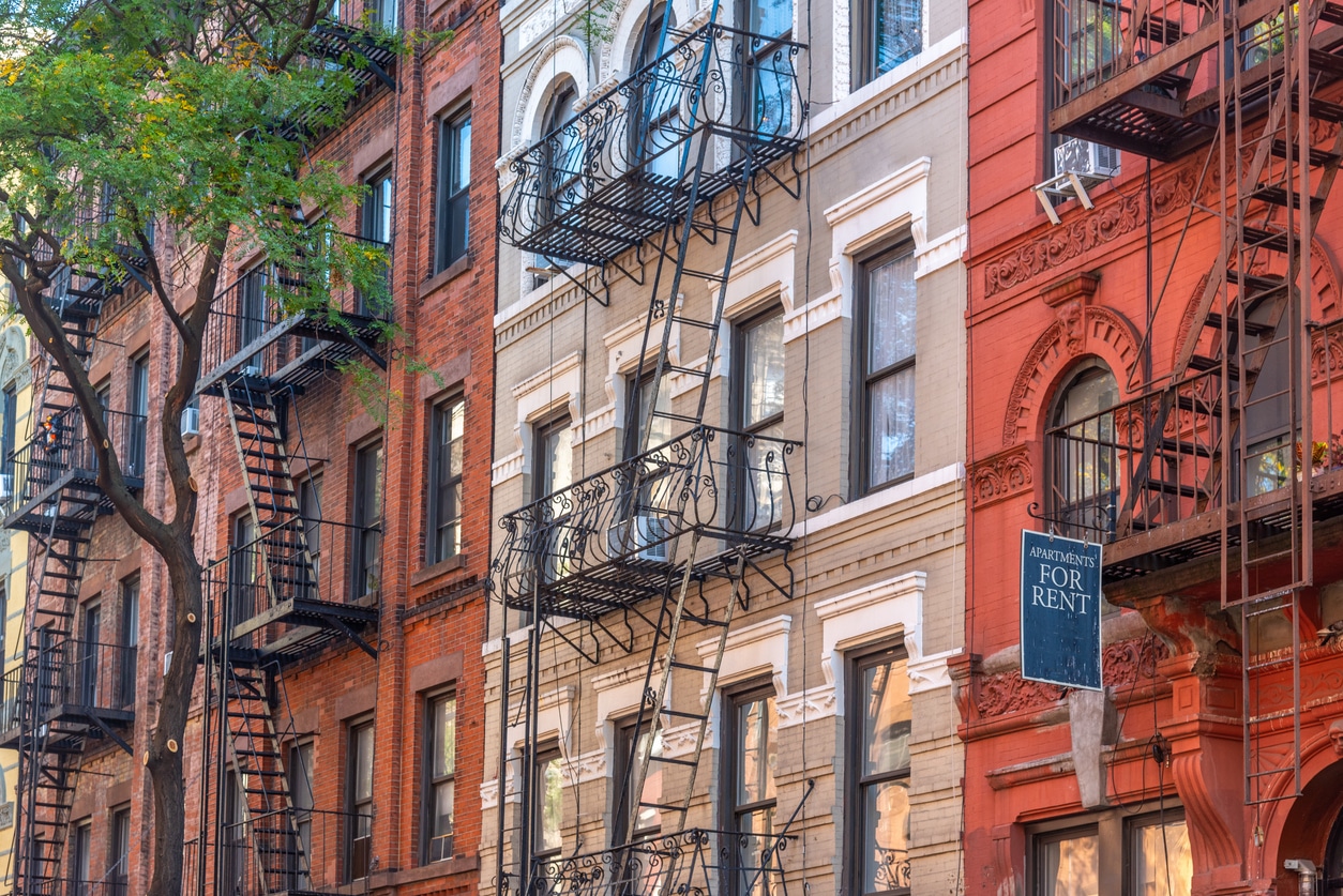 Row of classic New York City brick apartment buildings featuring black metal fire escapes