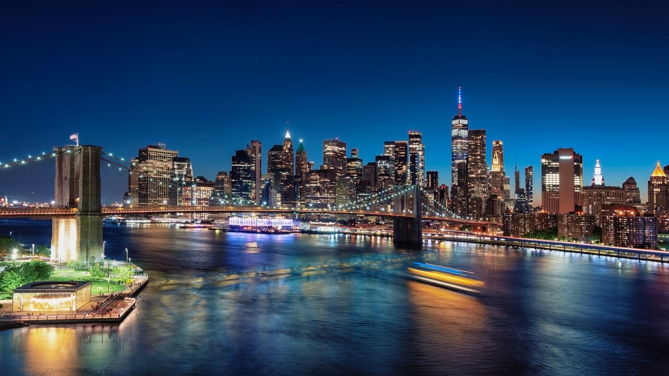 The Brooklyn Bridge and New York City skyline illuminated at night, greeting those moving from Miami to NYC