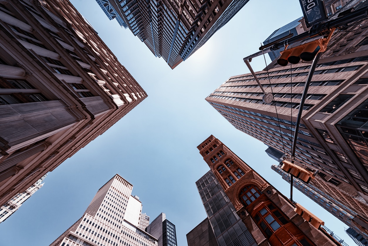 The skyline of New York City, United States Low-angle view looking straight up at various tall skyscrapers and traffic lights against a clear blue city sky
