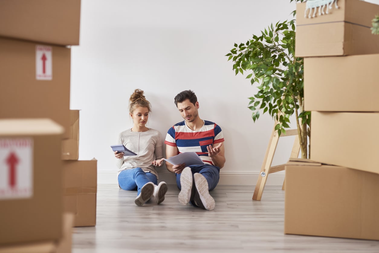 Worried couple examining expenses next to moving boxes A couple sits on the floor of an empty room, surrounded by moving boxes, as they get ready to move from Phoenix to Los Angeles