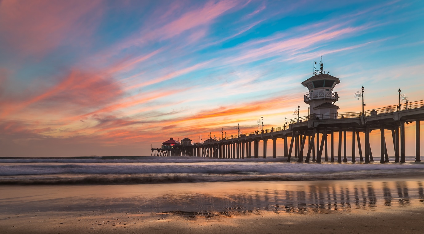 A long wooden pier stretching into the ocean beneath a vivid sunset, capturing the feeling of living in Orange County
