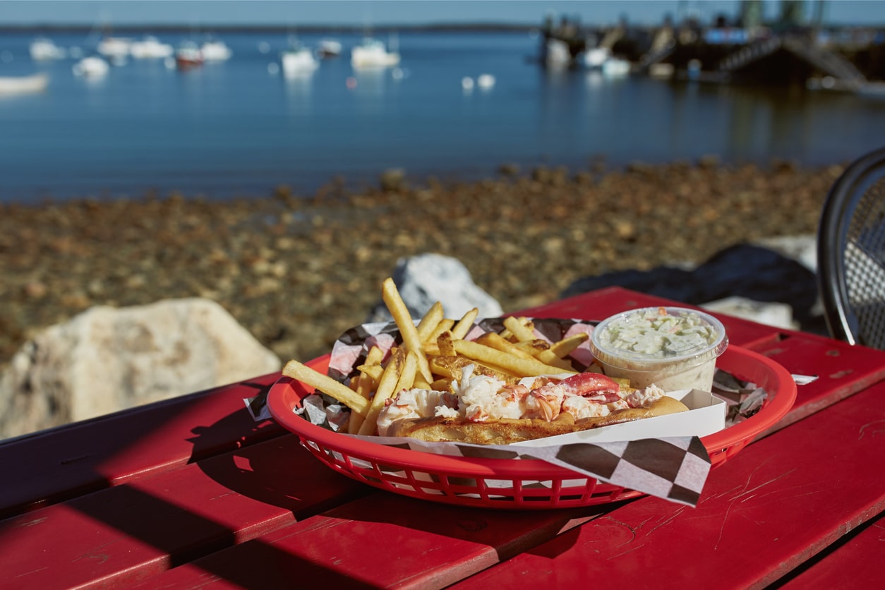 A classic Portland, Maine-style meal of a lobster roll with fries and coleslaw, served in a red basket