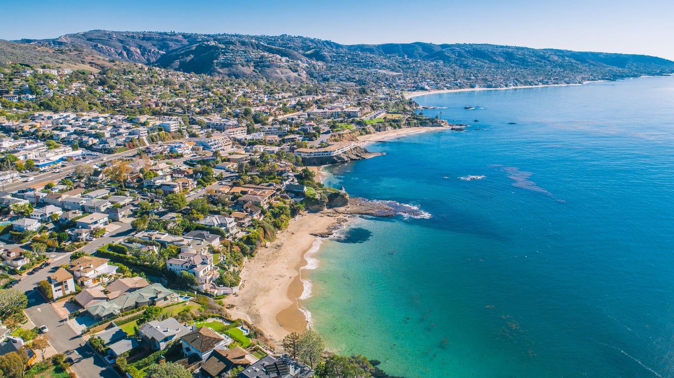 Aerial view of a coastal town in Orange County with luxury homes overlooking a sandy beach and turquoise water