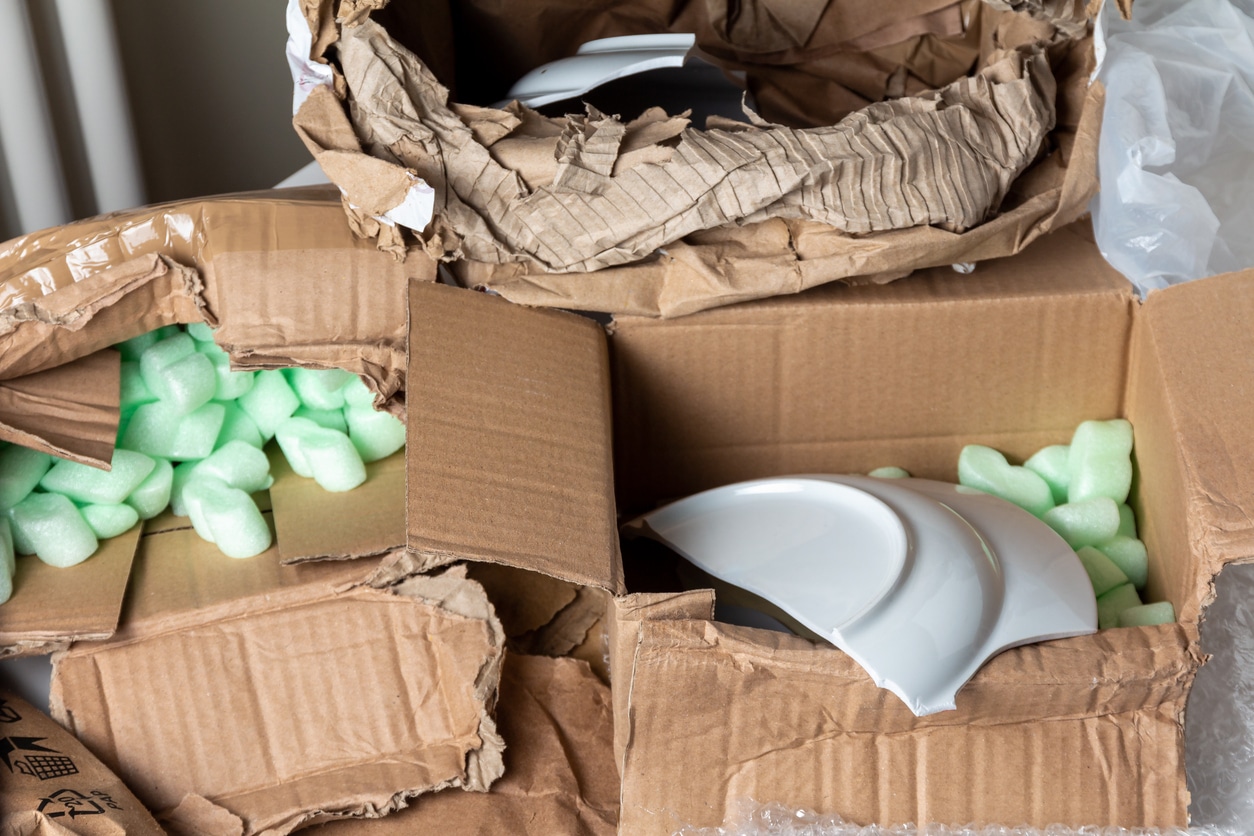 Broken white ceramic plates inside damaged cardboard boxes filled with green packing peanuts