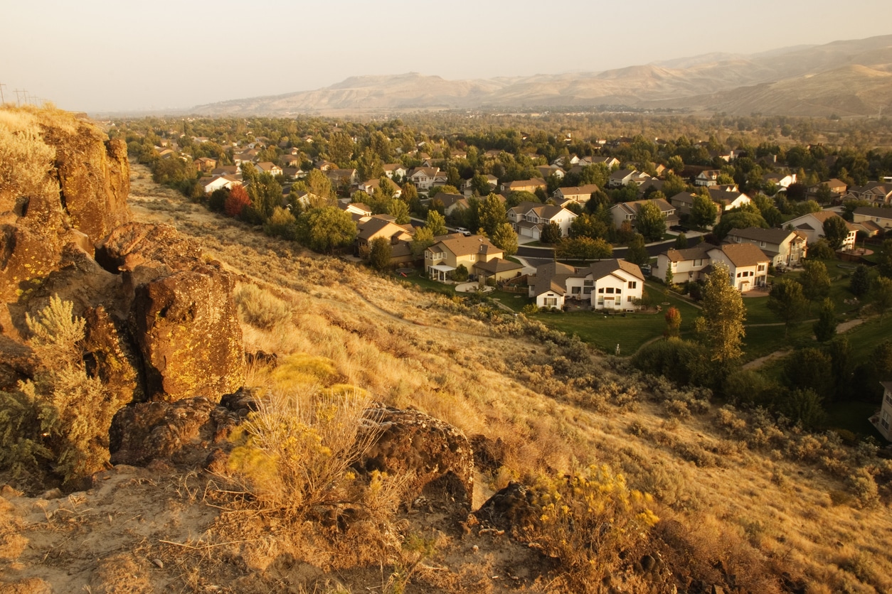 Sunlit homes sit on the foot of a steep, grassy hillside, one of the beautiful views available to those living in Idaho