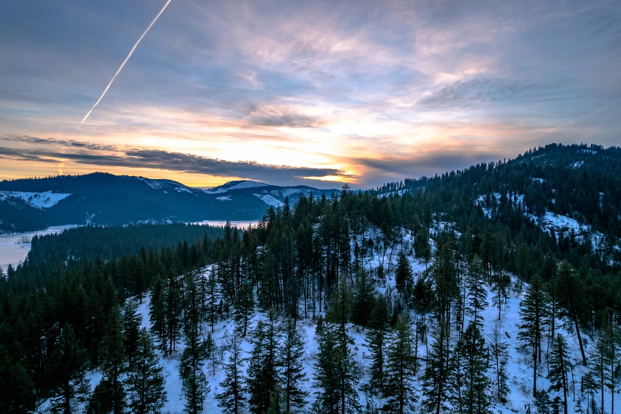 Snow-covered, pine-forested hills under a colorful sunrise sky, a sight those moving to Idaho can look forward to