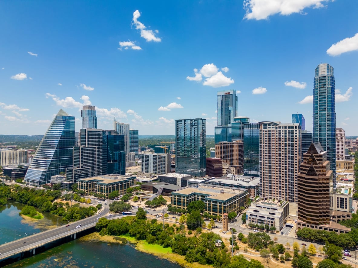 An aerial view of a downtown Austin next to a river under a clear blue sky with light clouds