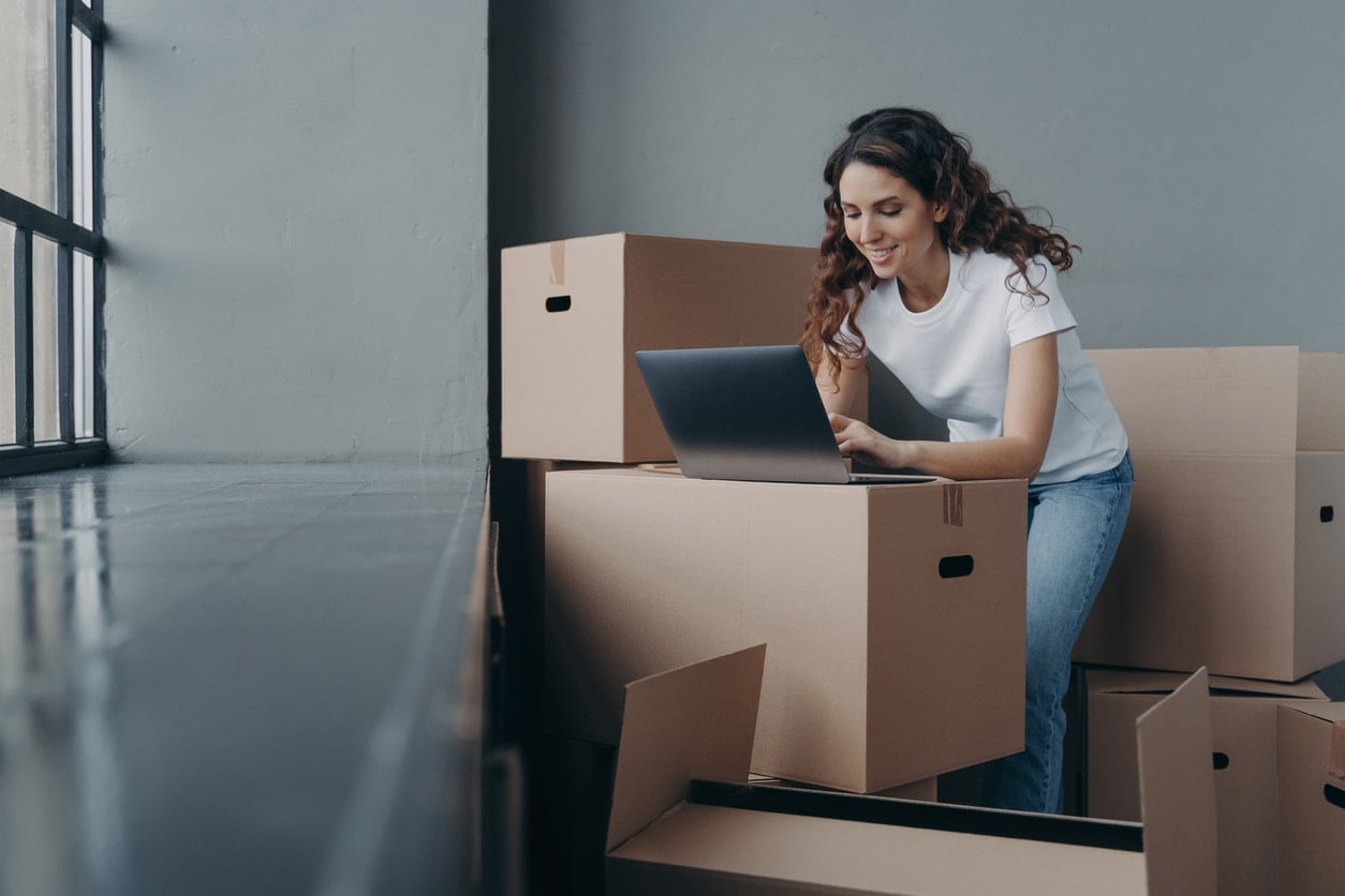 A smiling young woman leans over a moving box as she plans her move to one of the best cities for young professionals
