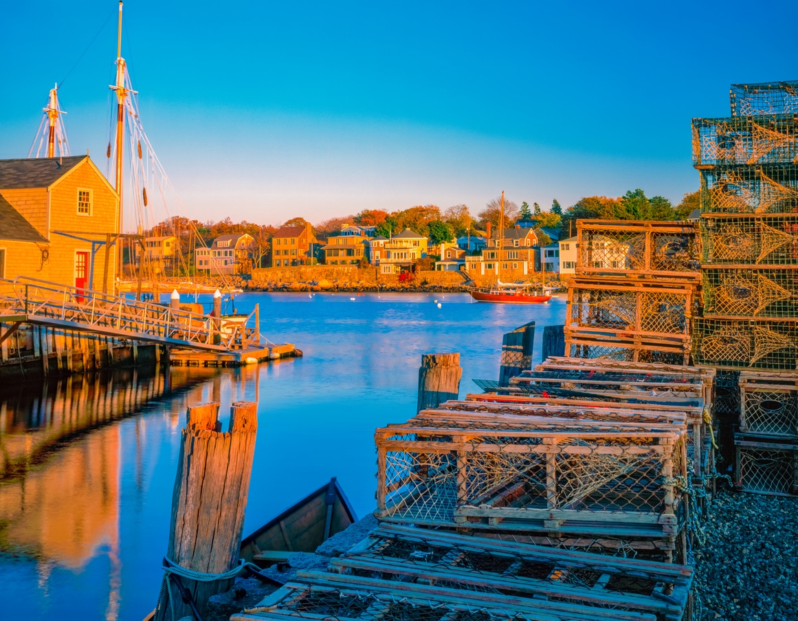Rockport Harbor and village with its lobster baskets glow in the sun. Wooden lobster traps stacked on a sunlit pier overlooking a calm harbor in one of the best places to live in New England