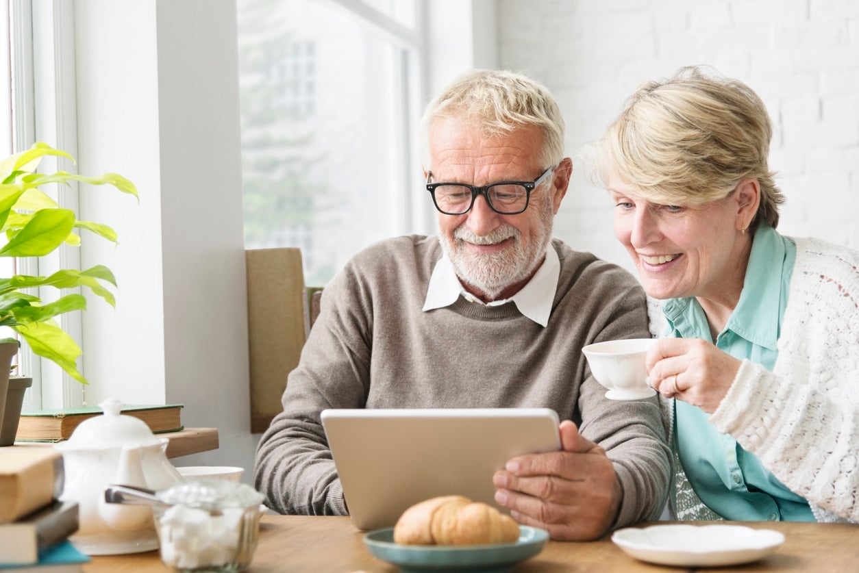 Senior Adult using Digital Device Tablet Concept A smiling older couple sits at a bright table as they plan how to downsize their home for retirement