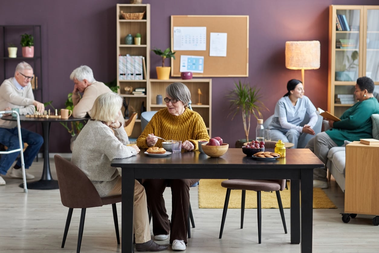Common room in retirement home with seniors enjoying leisure activities Several older adults relax and chat in a bright, modern retirement home lounge with comfortable seating and bookshelves