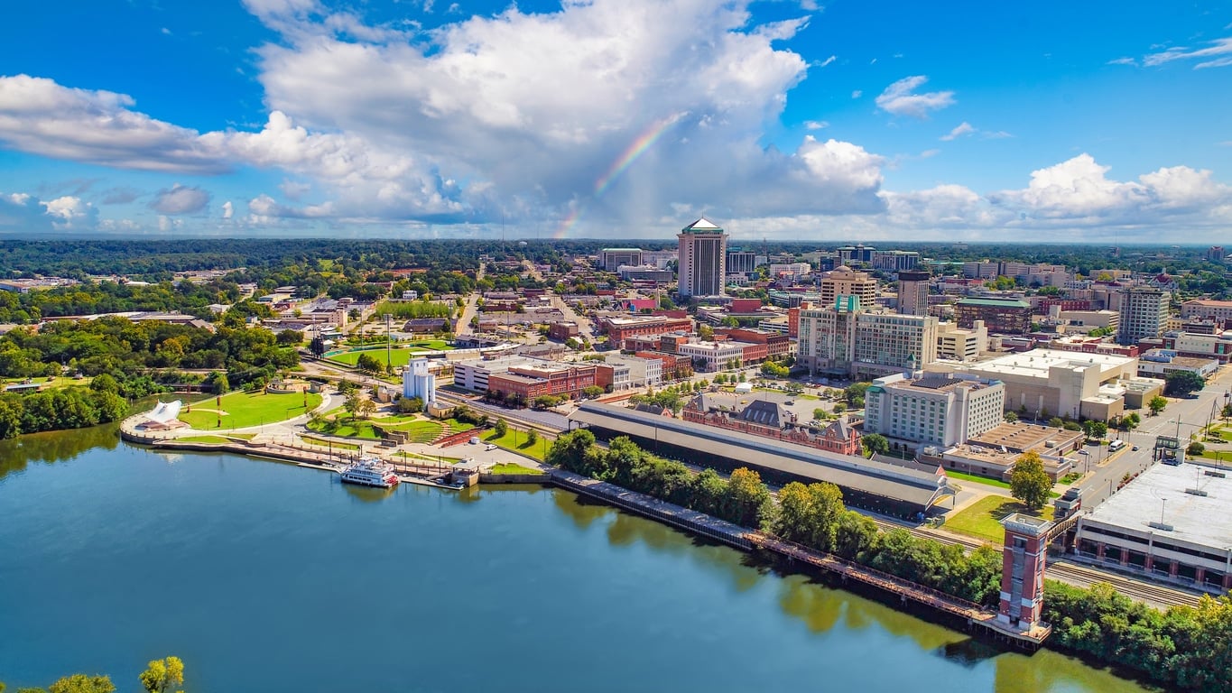 An aerial view of a riverside Alabama city under a bright blue sky with a vibrant rainbow