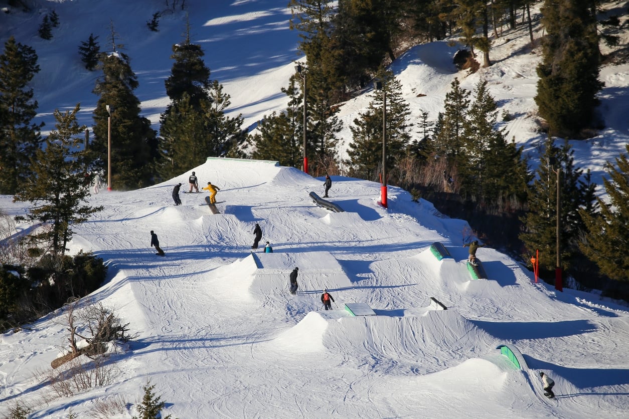 Skiers and snowboarders navigate ramps and rails at a snow-covered terrain park in Boise