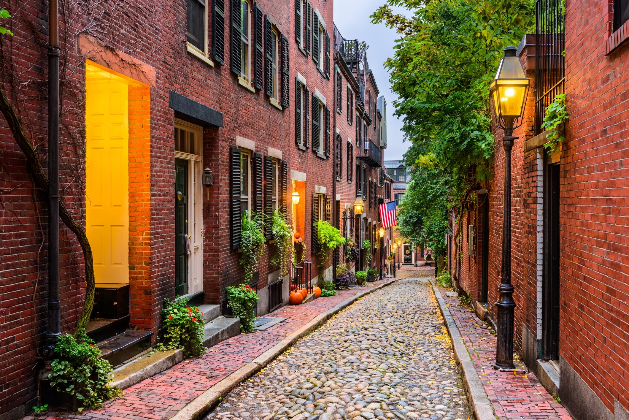 A narrow NYC cobblestone street lined with historic row houses and gas lamps awaiting those moving from NYC to Boston