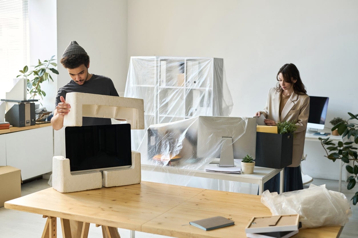 Business people packing things during the move A man places foam protectors on a computer monitor, demonstrating how to pack electronics for moving