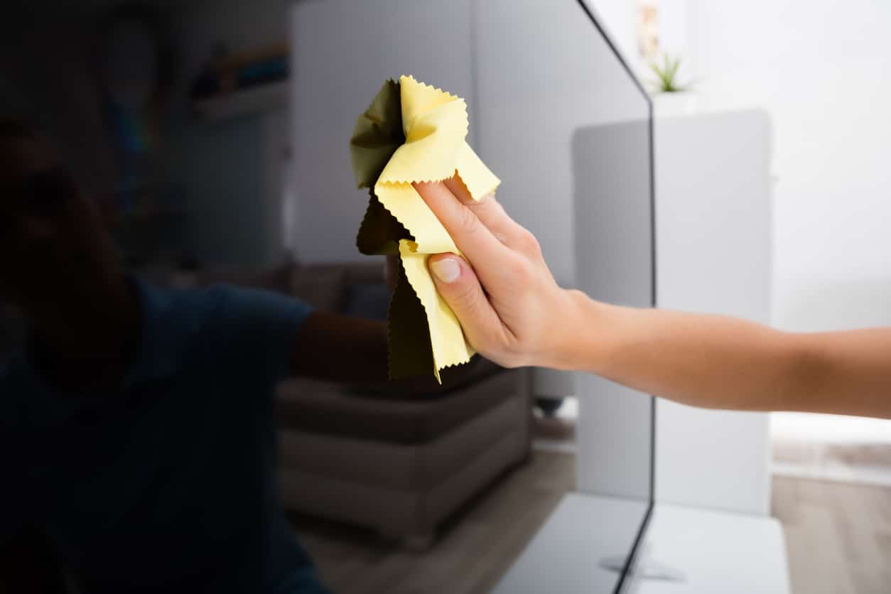 Woman Using Cloth To Clean The Television A close-up view of a person’s hand using a yellow microfiber cloth to prepare electronics for moving