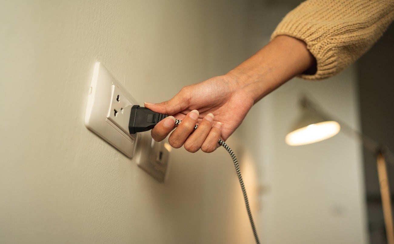 Close up woman hand put on or remove Electric plug cable in socket. Electrical equipment wires and power strips on the wall. Earth Hour saving energy. A person unplugging a black power cord from a white electrical outlet as part of packing electronics for a move